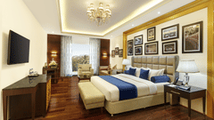 The executive suite bedroom with a king size bed, seating area, television, wooden flooring, framed wall decor and elegant lighting at La Marvella, Bengaluru.