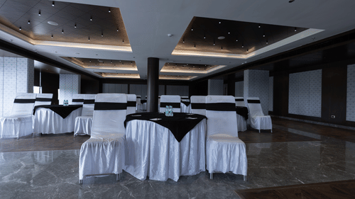 A spacious banquet hall at Pride Resort, Jodhpur, set up with tables and chairs covered in white and black cloth.
