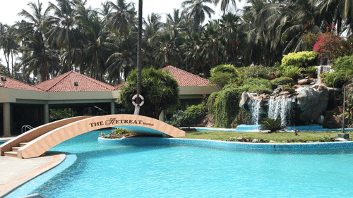 A view of the pool at The Retreat Hotel and Convention Centre with a bridge, canopies and trees in view