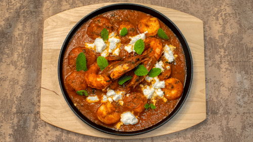 A round bowl filled with curry and garnished with herbs placed on a wooden board.
