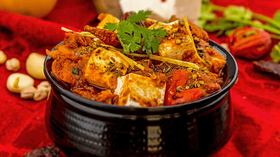 Traditional Indian paneer curry served in a black handi pot garnished with coriander and whole spices.