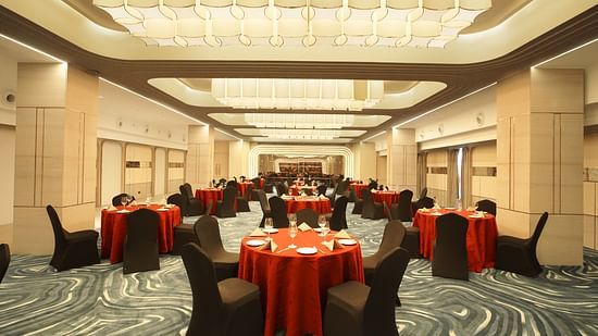 Warmly lit banquet room with round tables covered in red cloths and black chairs. Patterned carpet and soft lighting - The Orchid Hotel, Chandigarh