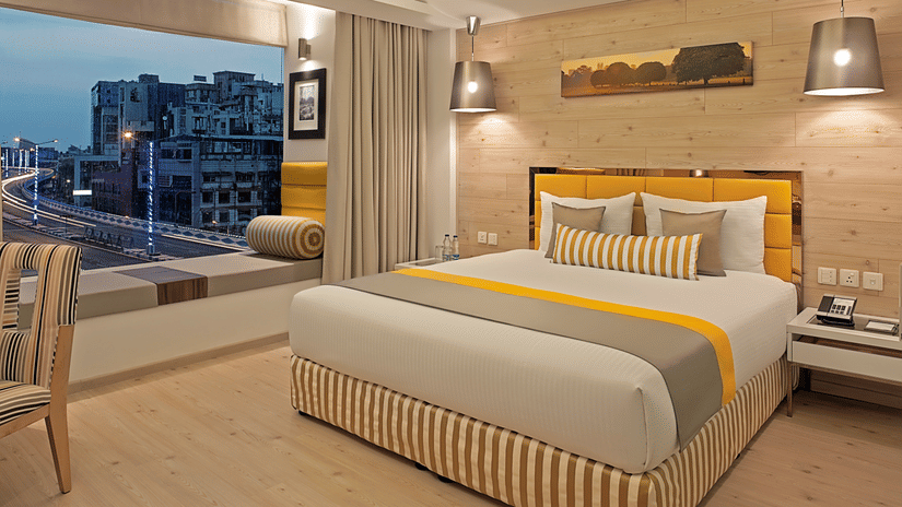 An elegantly designed Deluxe Room at Barsana Boutique Hotel, Kolkata, featuring a well-made bed along with a floor-to-ceiling window offering city views.