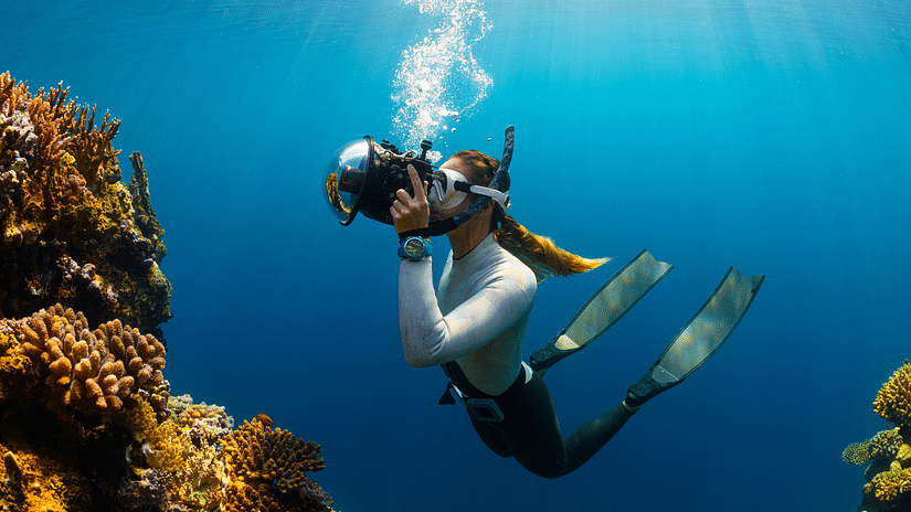 A diver swims amidst vibrant coral, with bubbles rising in clear blue water, capturing a dynamic underwater scene.