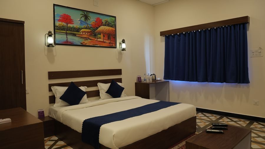 Interior of a room at VITS Select Diamond Resort, Sasan Gir with a double bed, side table, painting, and curtains.