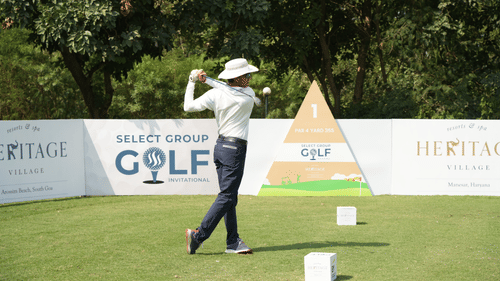 Golfer in mid-swing during a professional golf event with visible sponsor banners in the background.