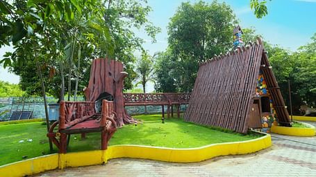 A charming garden scene at MGM Dizzee World featuring large wooden swings, a shaded hut-like structure, and well-maintained greenery — ideal for relaxation and photo opportunities amidst a vibrant outdoor setting.