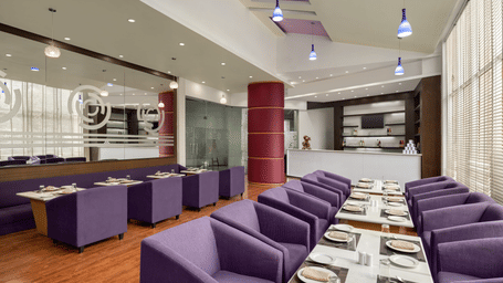 The Maya lounge at Ramada by Wyndham Bodh Gaya Mahabodhi featuring rows of neatly arranged tables and chairs with elegant modern interiors.