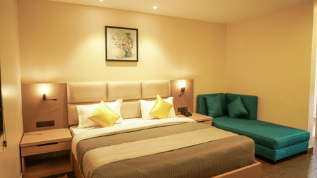 A stylish hotel bedroom featuring a double bed with yellow cushions and a teal chaise longue under warm lighting at Trident The Boutique Hotel, Ooty.