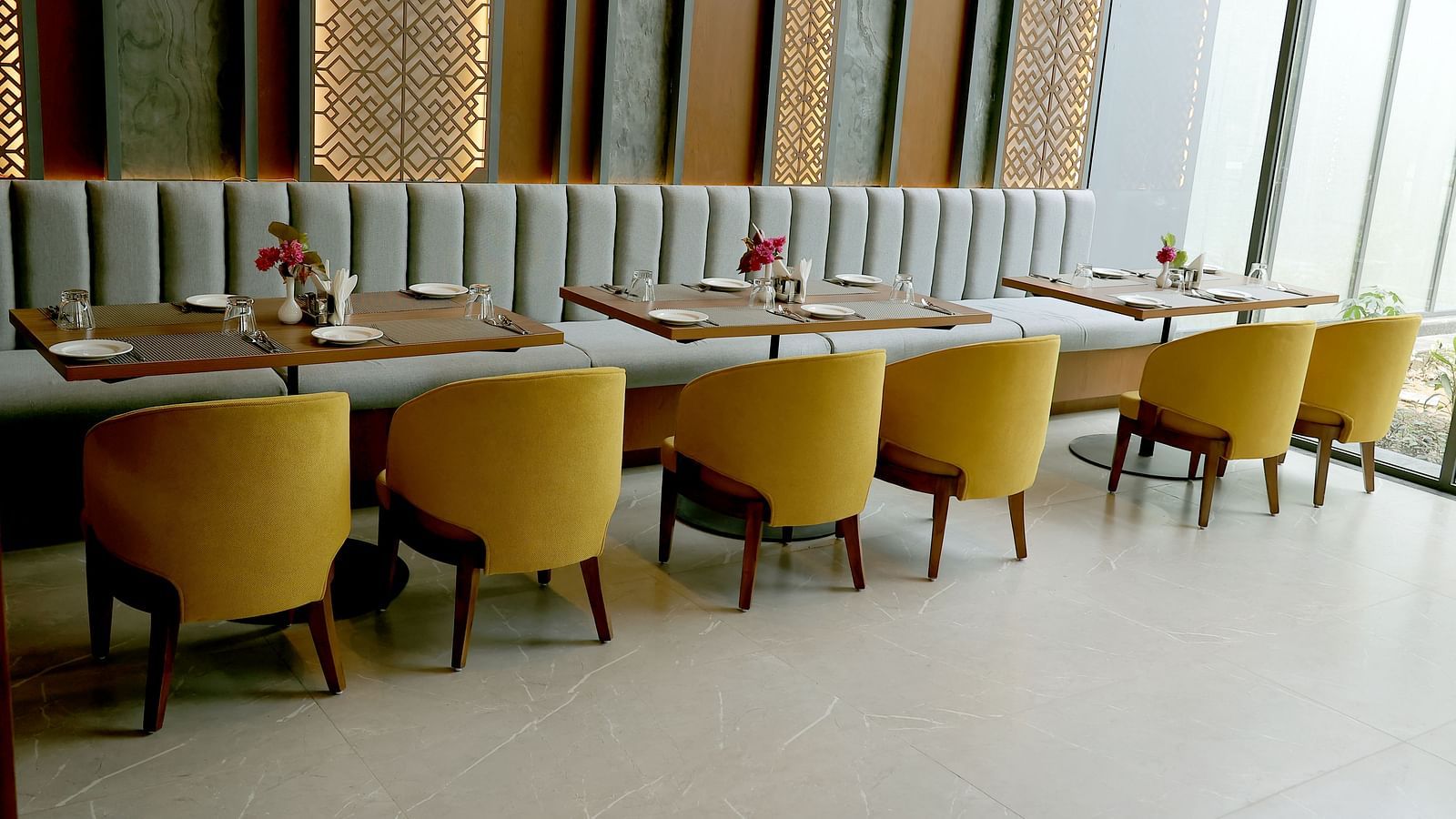Elegant indoor dining area with mustard yellow chairs and a striped cushioned bench against a decorative wall at Wyndham Garden.