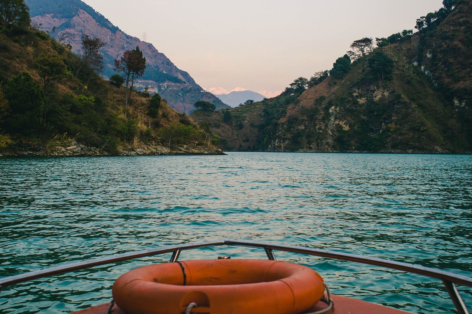 a boat decked with a orange tyre surrounded by mountains