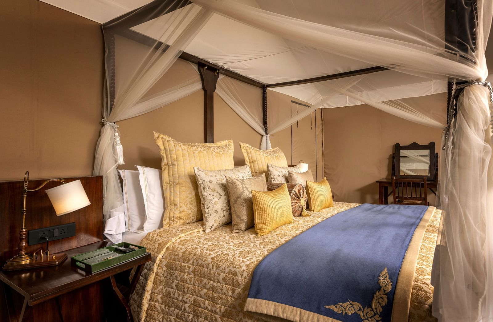 A large bed with pillows covered in golden coloured sheets and a lamp on a night stand by the side - Aalia Jungle Resort & Spa
