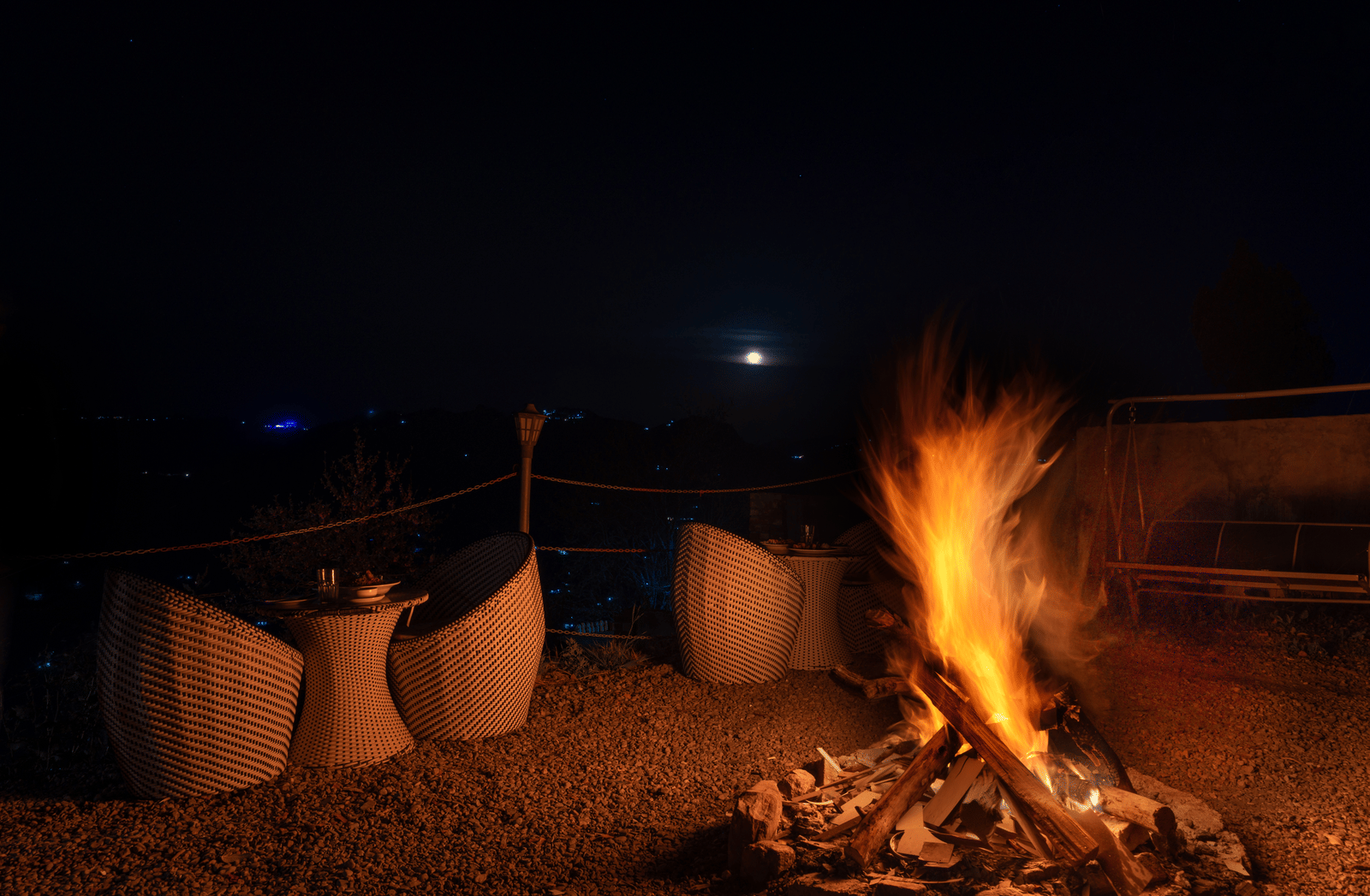 A glowing bonfire at night surrounded by comfortable outdoor chairs under a dark sky at Himalayas Resort By The Lake Hill, Mukteshwar.