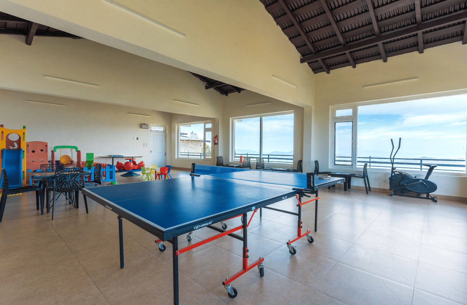 An indoor recreation area with a table tennis setup and windows overlooking the view at Himalayas Resort By The Lake Hill, Mukteshwar.