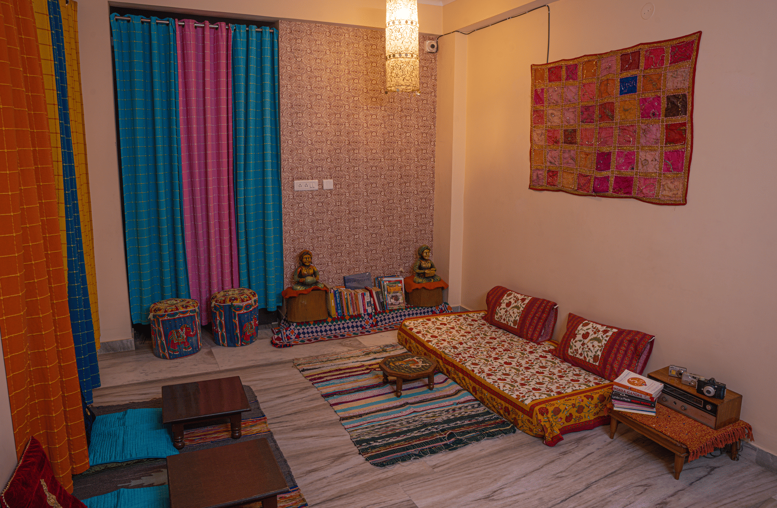 A room with a low bed, cushions, wall hanging, floor seating, and decorative items at Jaypore360 Homestay in Jaipur.