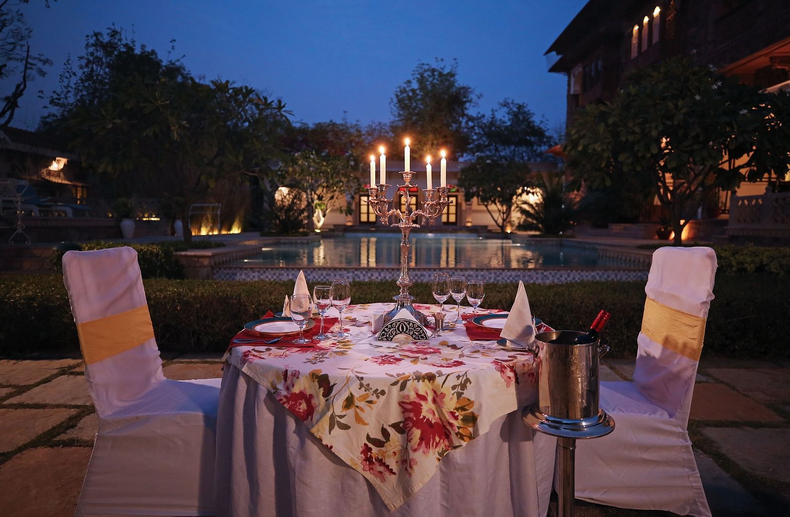  A table set for a romantic dinner by a swimming pool at dusk, illuminated by candles - Khas Bagh, Jaipur.
