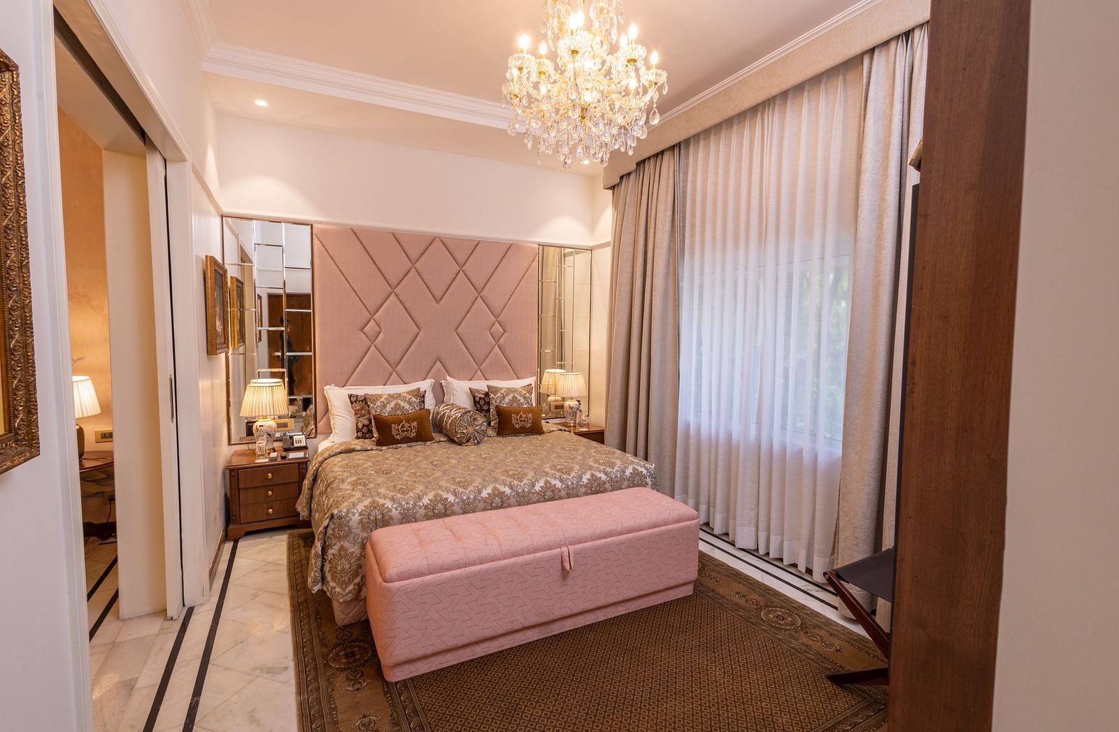 Luxury Suite at The Claridges New Delhi, featuring a cosy king sized bed with pillows and an elegant chandelier hanging overhead