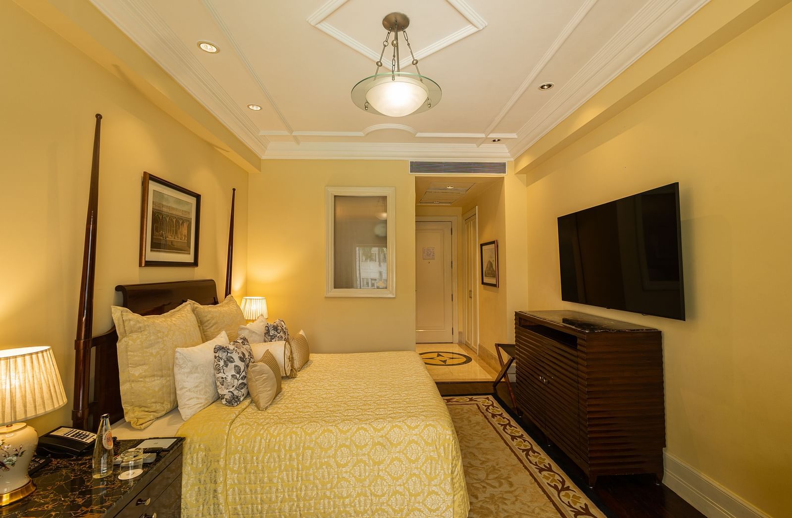 Side view of the Deluxe King Bed Room Pool View at The Claridges New Delhi, featuring a cosy king sized bed, wall-mounted TV, and bedside lamps