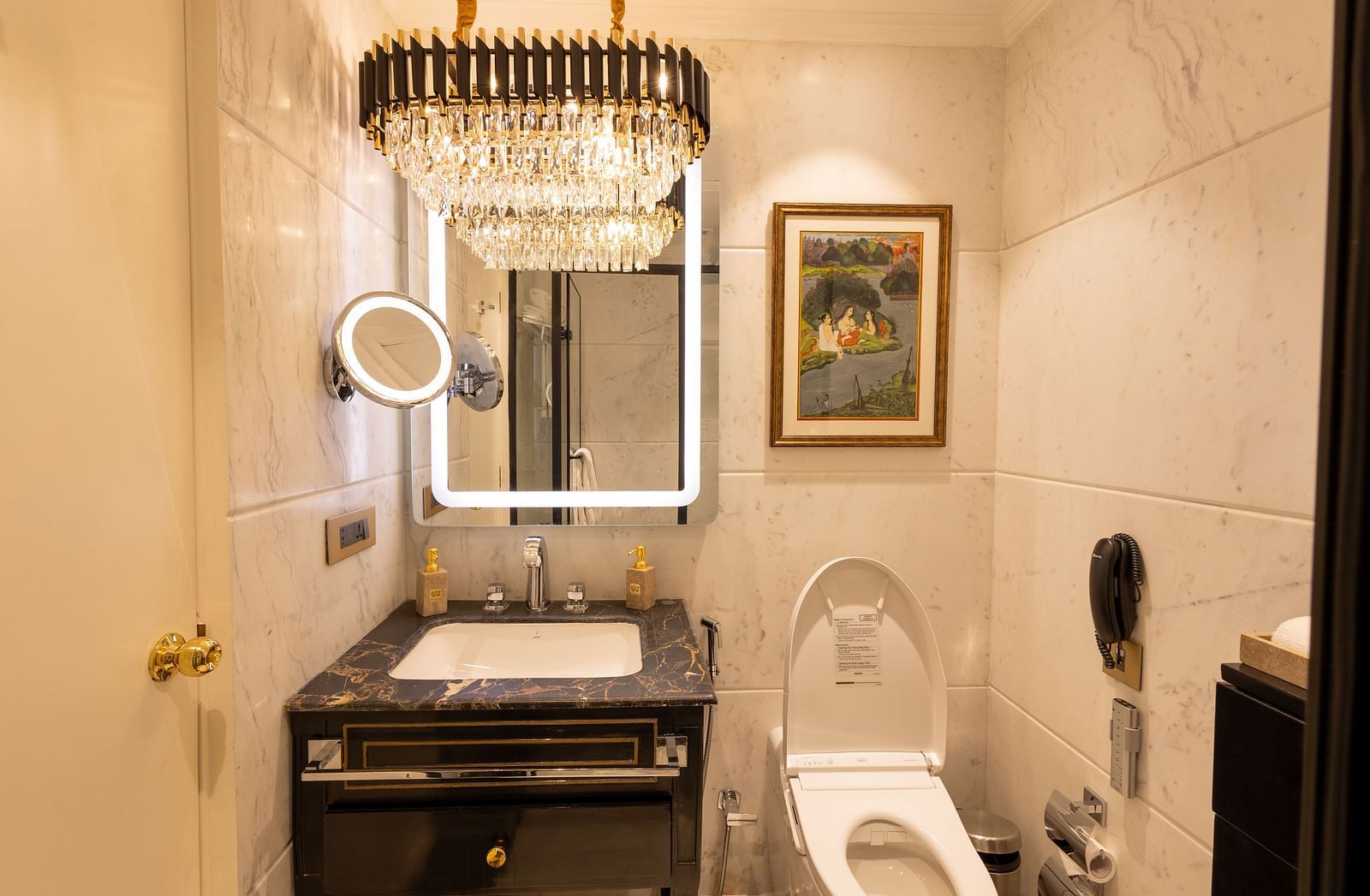 Luxury Suite washroom at The Claridges New Delhi, featuring a stylish sink, wall-mounted mirror, and a chandelier