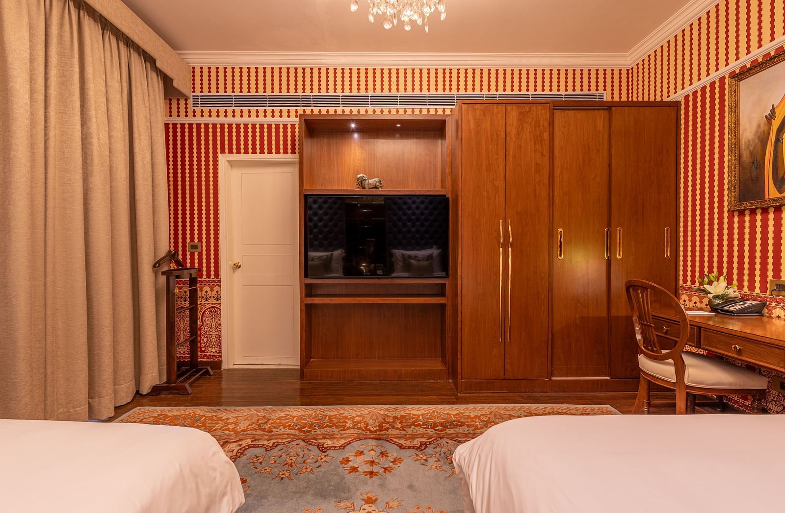 Spacious Luxury Twin Bed Room with Balcony at The Claridges New Delhi, featuring two separate beds, a stylish candellia hanging, and a wall-mounted TV