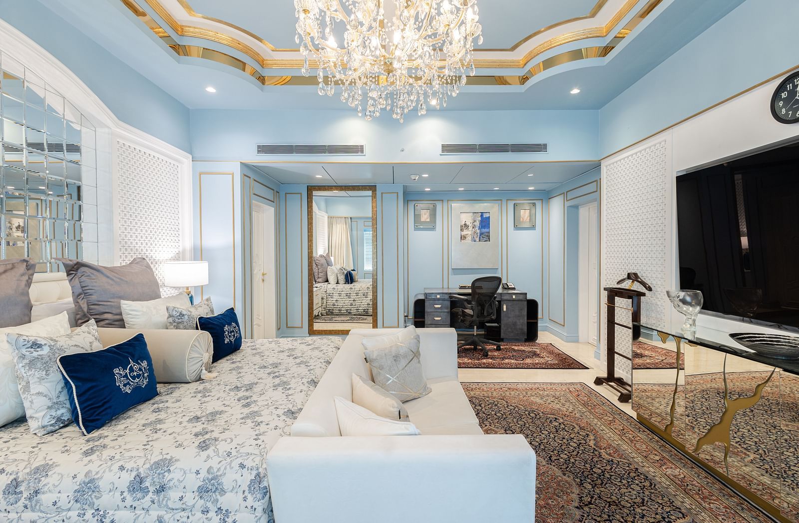 an image of our diplomatic suite room with a large bed with pillows, a couch in front of a television under a chandelier - The Claridges New Delhi
