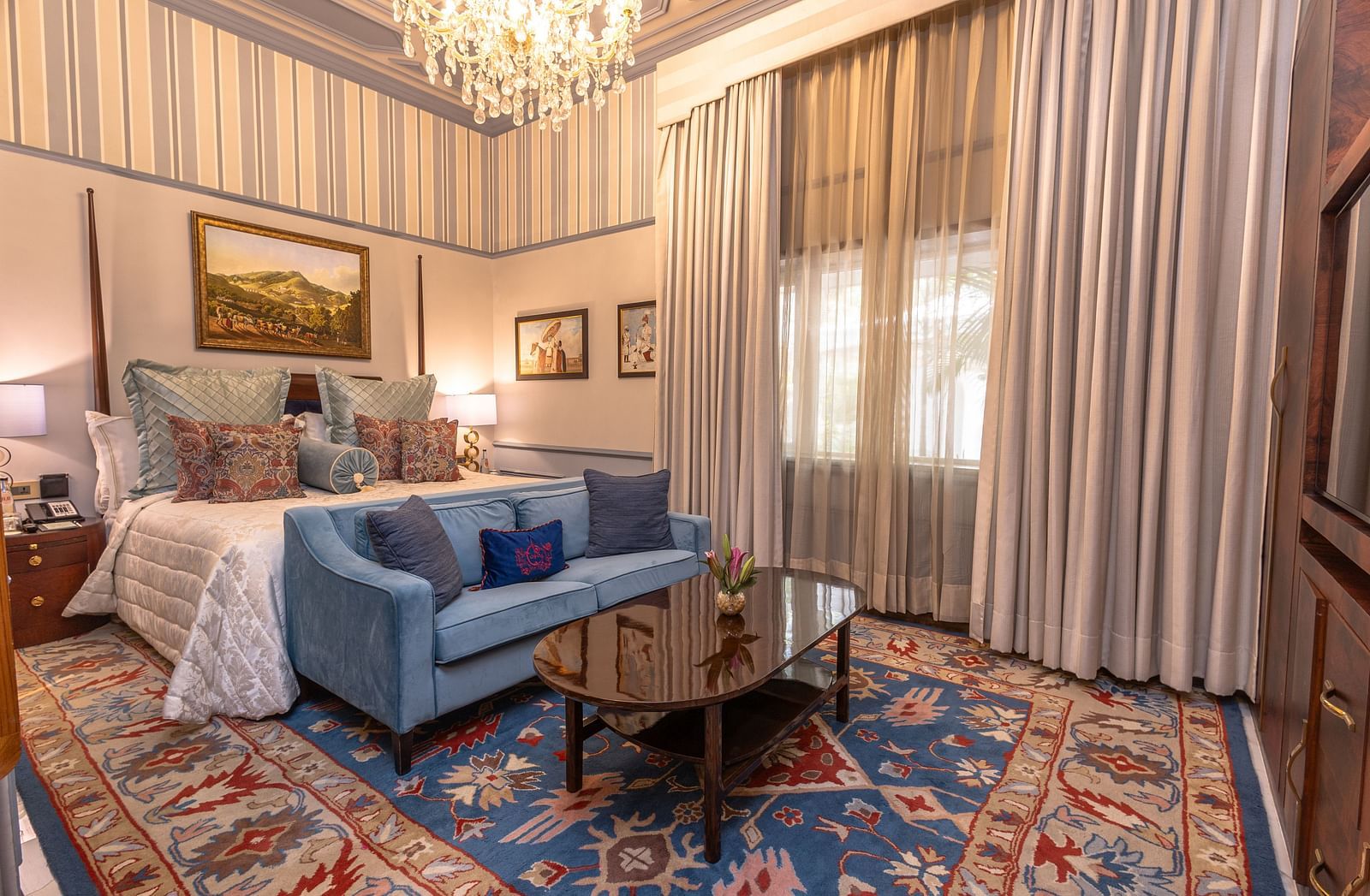 image of the brightly lit bedroom with a king size bed and blue couch place in front of the bed at our heritage parlour suites - The Claridges New Delhi