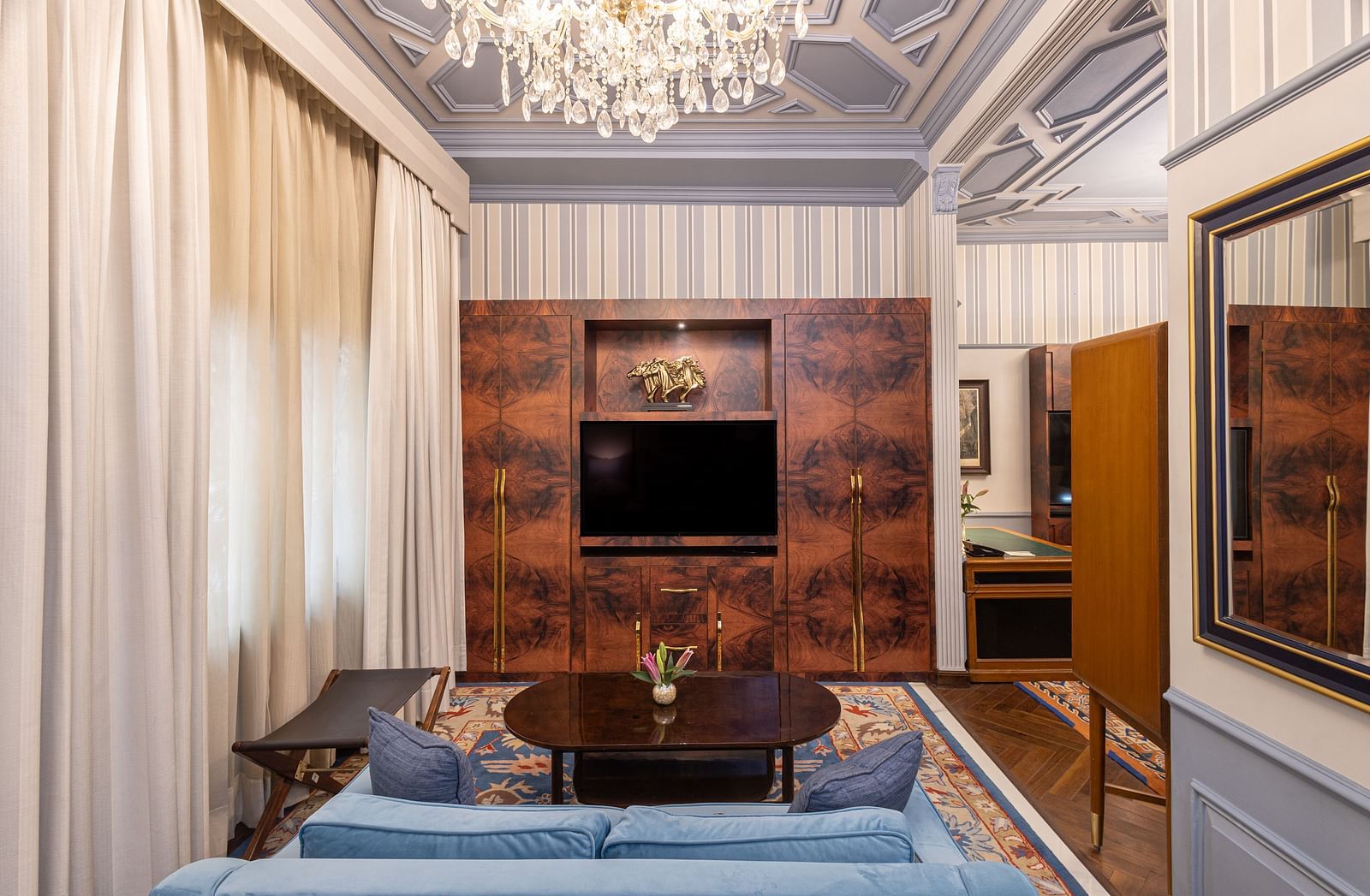 image of the bedroom with a wall mounted television placed in front of the bed with a light blue coloured couch at our heritage parlour suite - The Claridges New Delhi