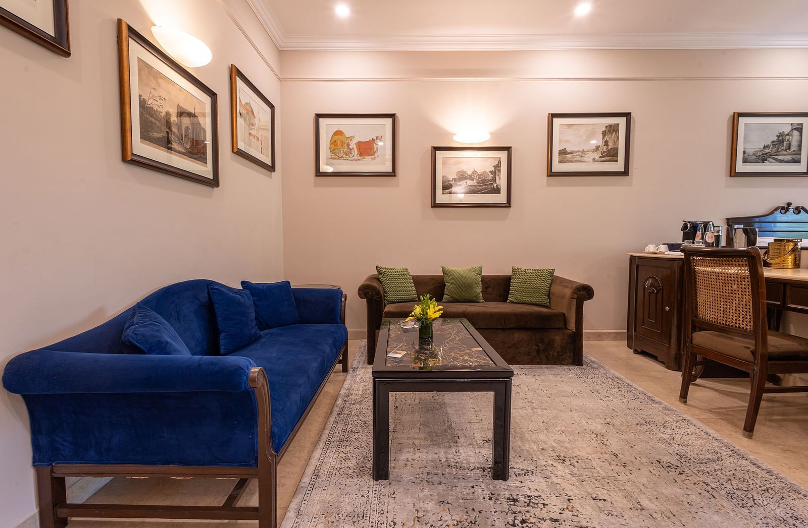 Corner view of the Grand Luxury Twin Bed Room at The Claridges New Delhi, featuring a cosy sofa with a table in front and framed photos on the wall