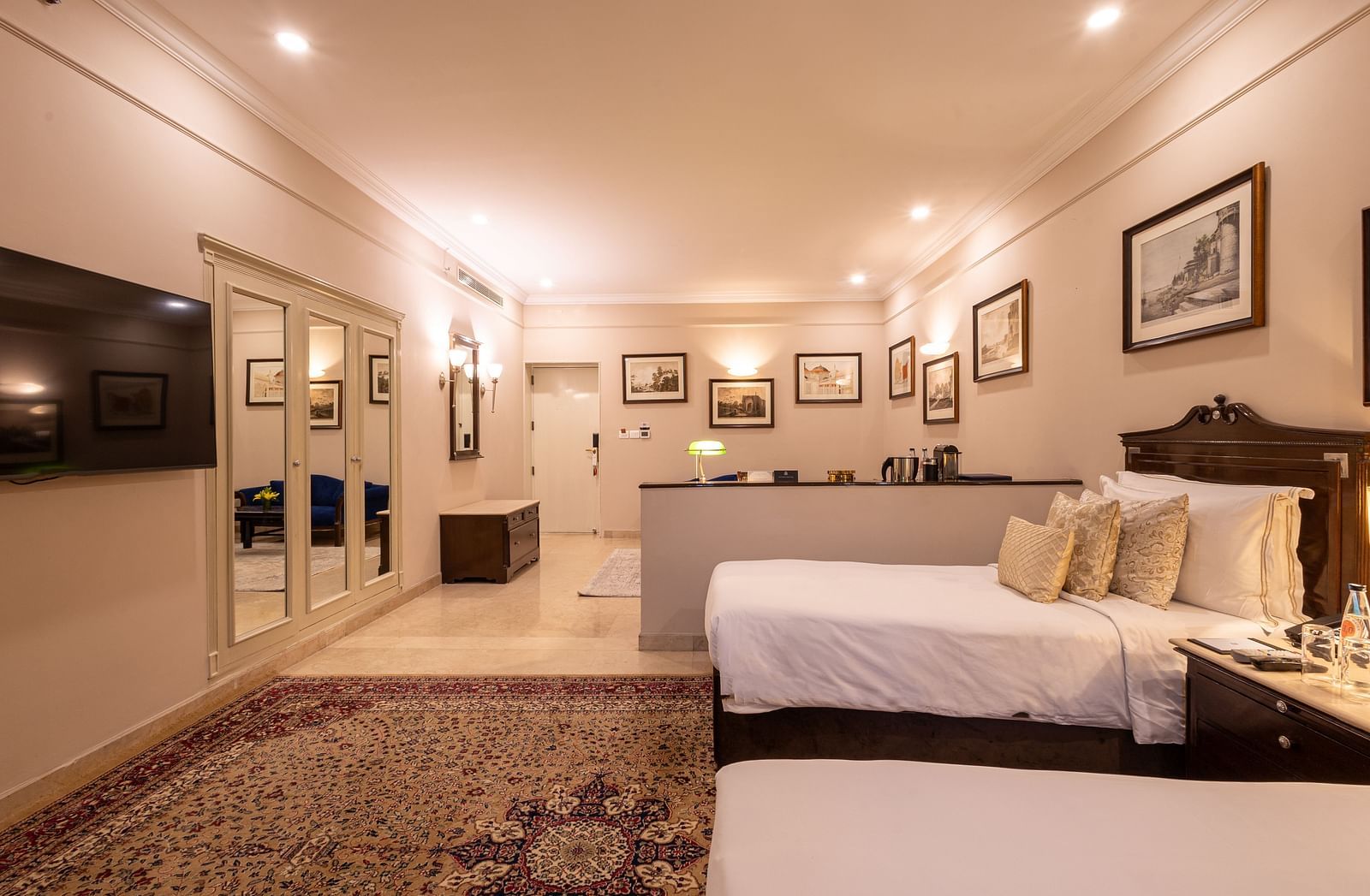 Side view of the Grand Luxury Twin Bed Room at The Claridges New Delhi, showcasing a spacious layout with framed photos on the wall and an elegant lighted ceiling