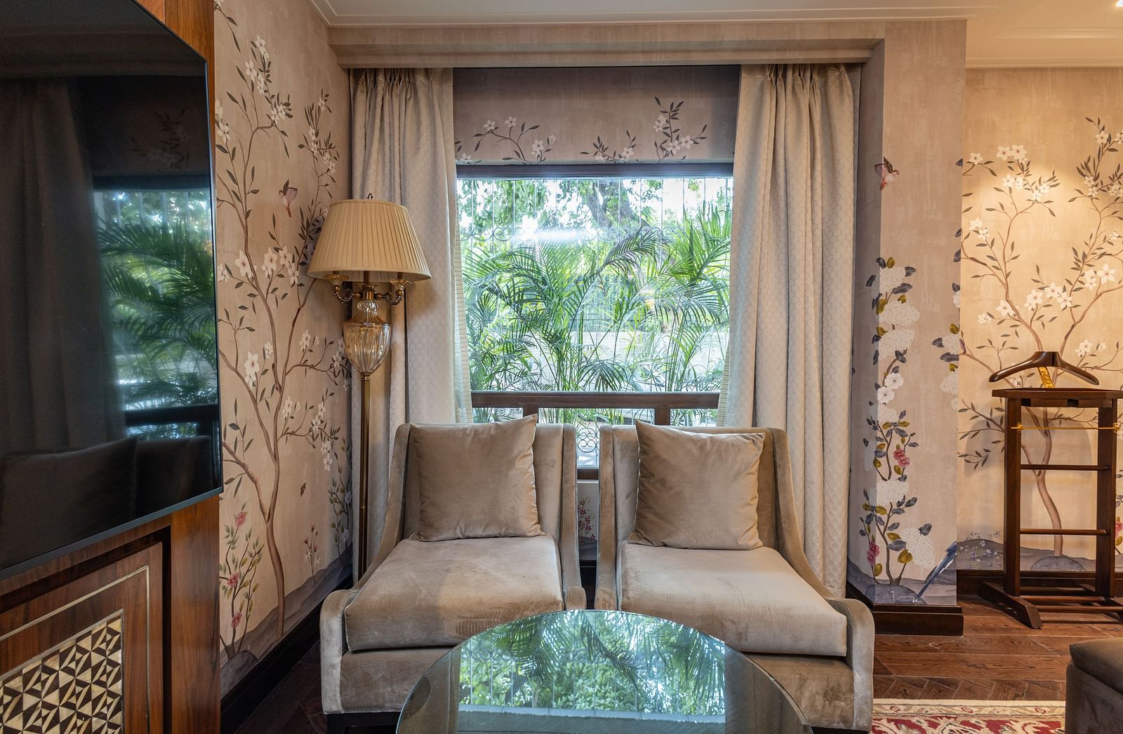 image of two single seater couch seats grey in colour with a huge window behind it at our cabana room - Image of the Cabana Room featuring two single-seater couches and a wall-mounted television - The Claridges New Delhi