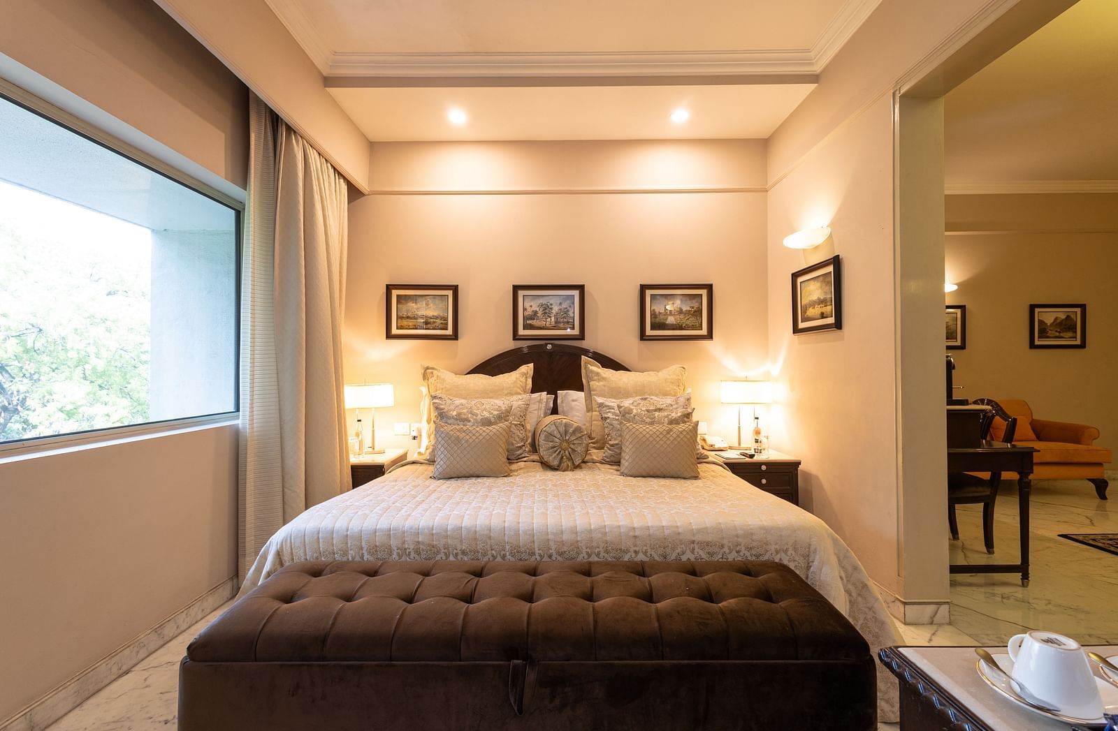 a close up view of the bed of the heritage parlour room with a brown seating arrangement in front of the bed - A distant view of the bed with a partition in the Heritage Parlour Rooms at The Claridges New Delhi