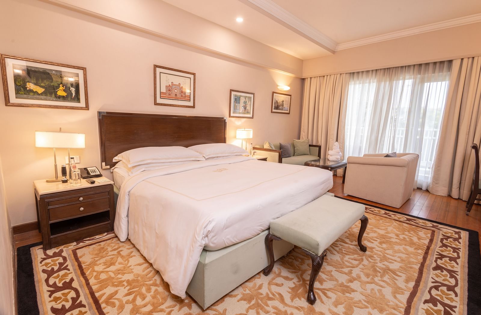 side angle view of the heritage balcony room with a plush comfortable king size bed and a cushioned stool in front of it - The Claridges New Delhi