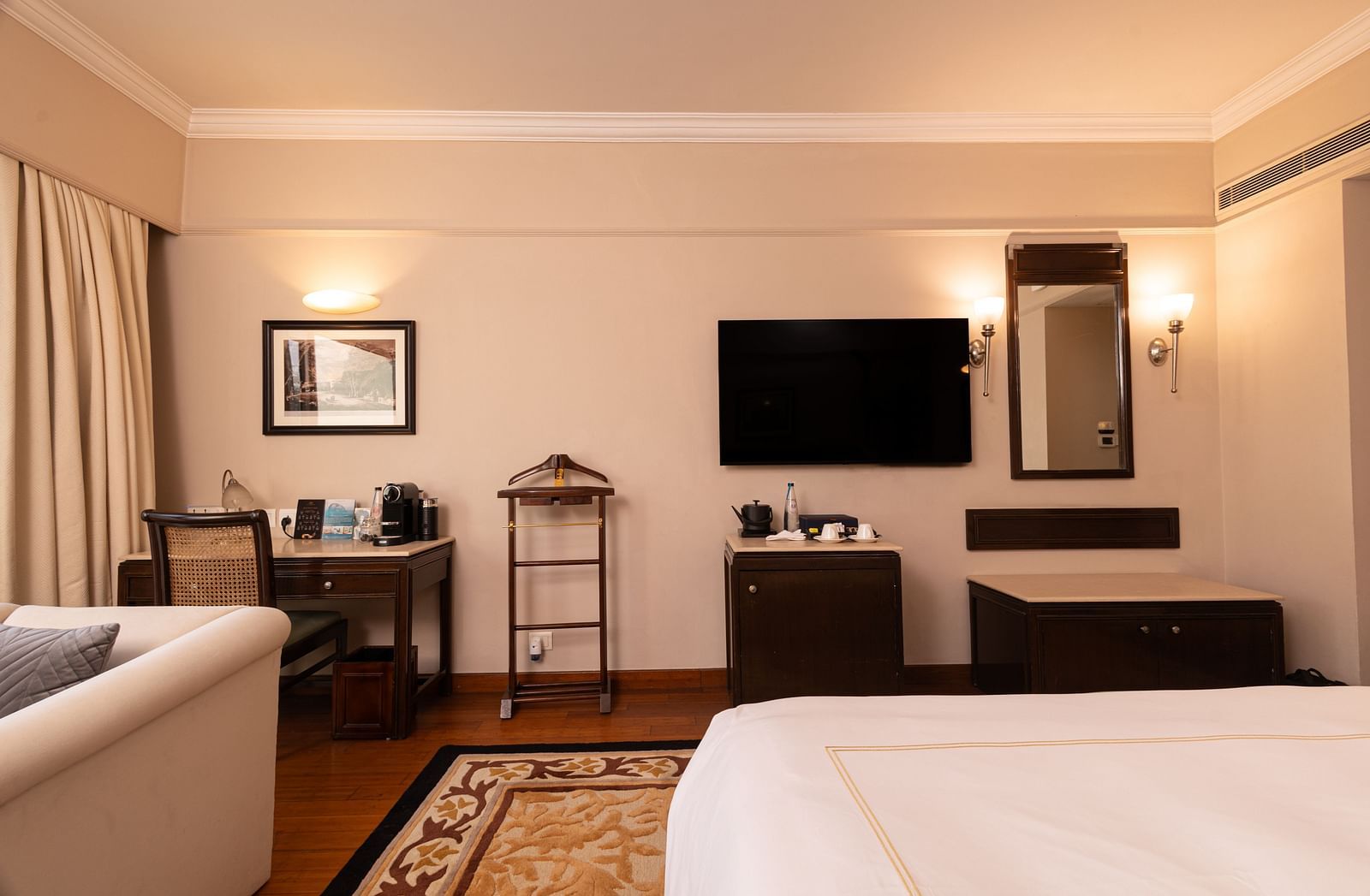 inside view of the heritage balcony room with a wall mounted tv in the middle, and a mirror along with a work desk besides it - The Claridges New Delhi