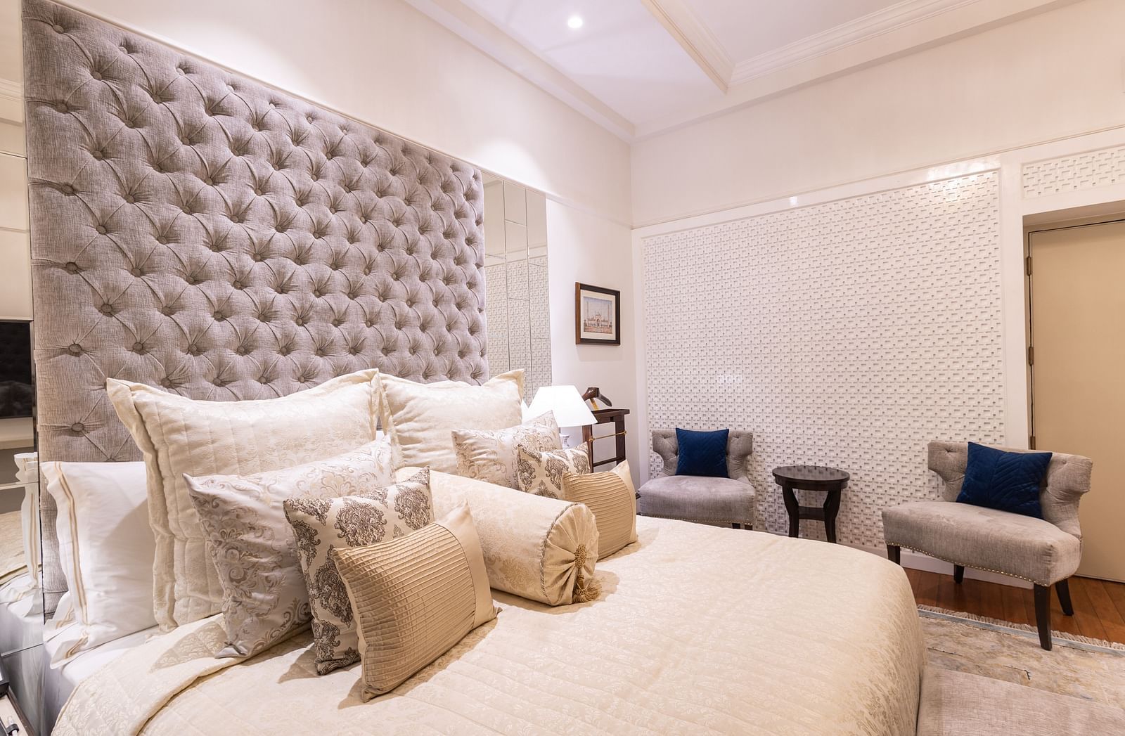 a side angle view of the boutique room with a well decorated king size bed and two cushioned chairs in the background - The Claridges New Delhi