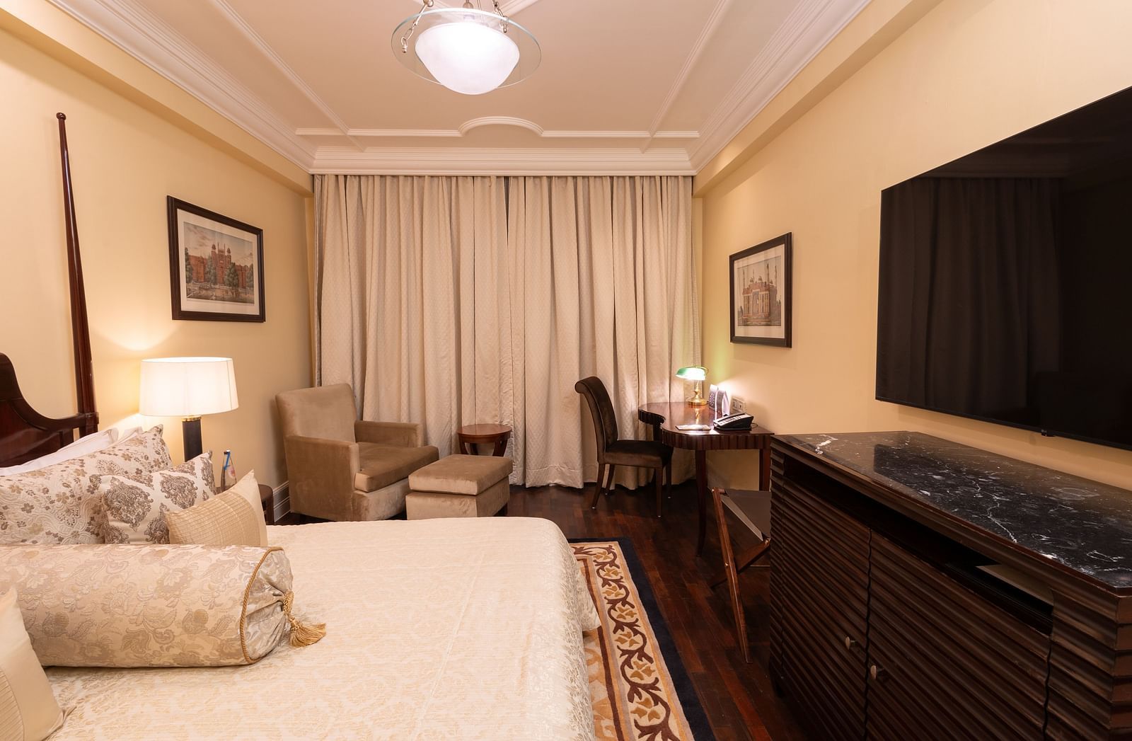 full view of the heritage parlour rooms with a plush king sized bed and a wall mounted tv screen placed in front of the bed at our heritage parlour rooms - The Claridges New Delhi