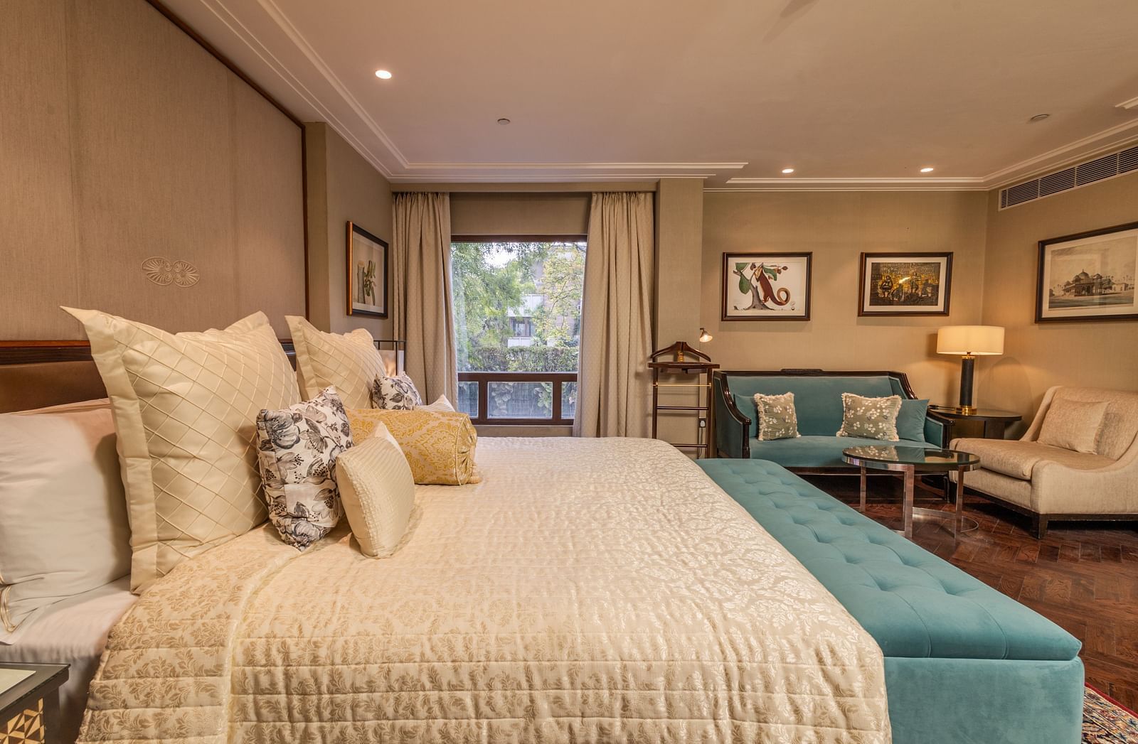 Image of a plush king-size bed adorned with a soft comforter, with a window in the Cabana Room - The Claridges New Delhi