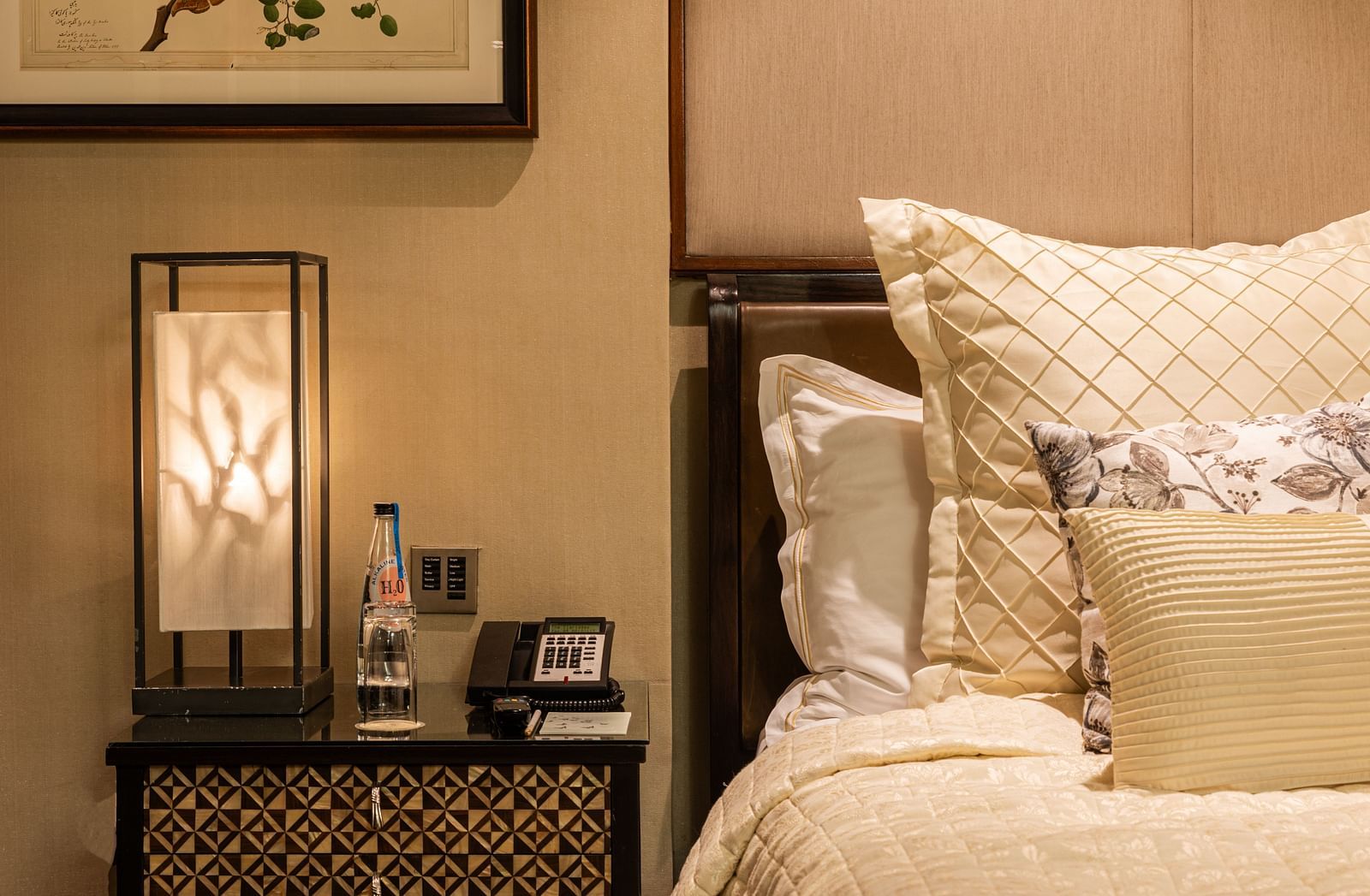 a closeup shot of the side table besides the bed featuring a night lamp and the soft pillows on the bed at the cabana room - The Claridges New Delhi