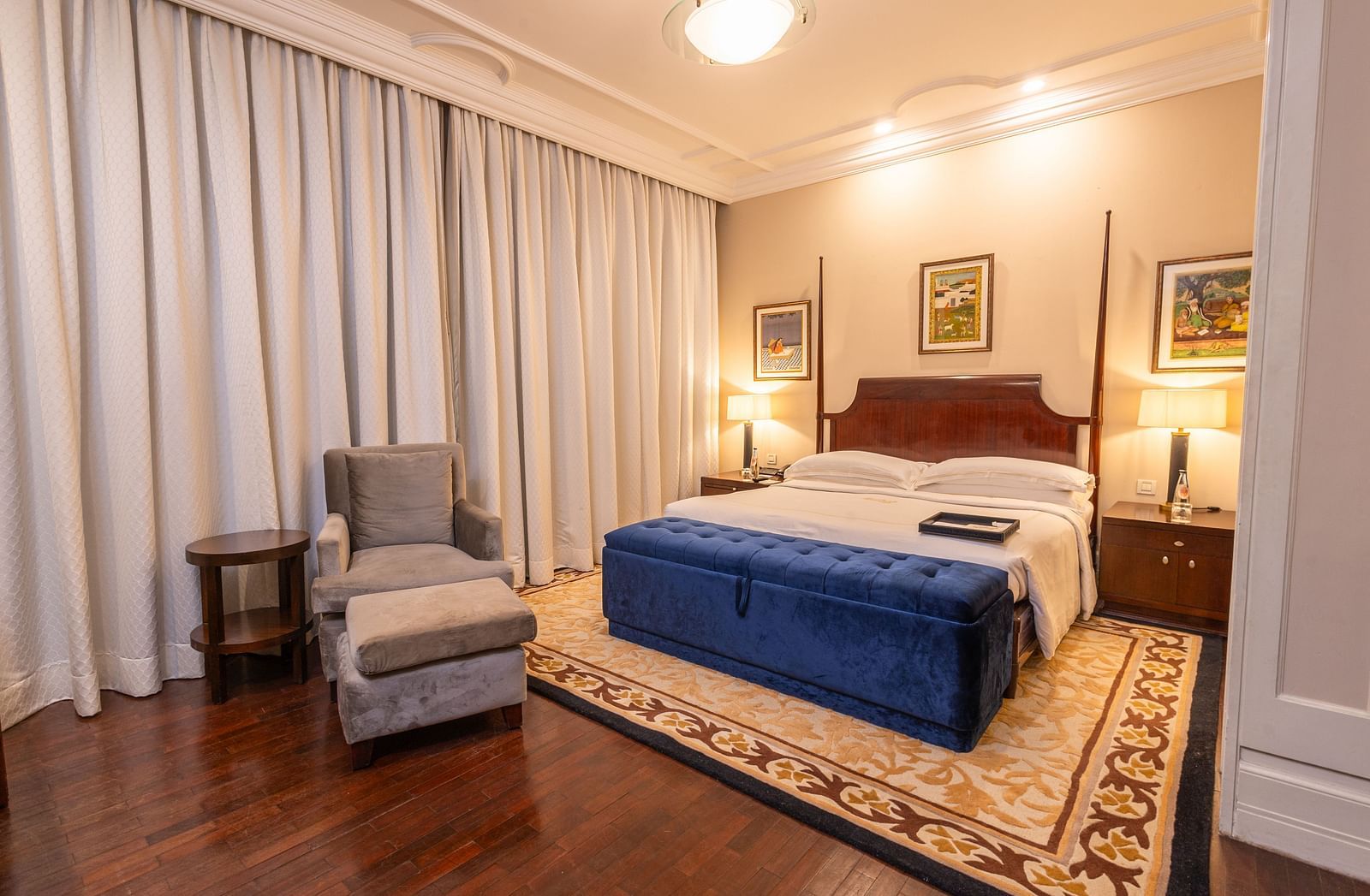corner view of the luxurious bedroom at our heritage rooms with white curtains and a grey arm chair  - The Claridges New Delhi