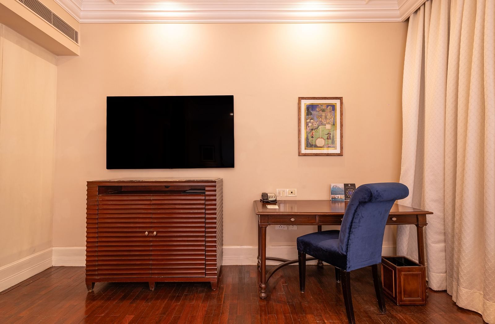 image of a wall mounted television and a work desk with a blue chair at the heritage room - The Claridges New Delhi