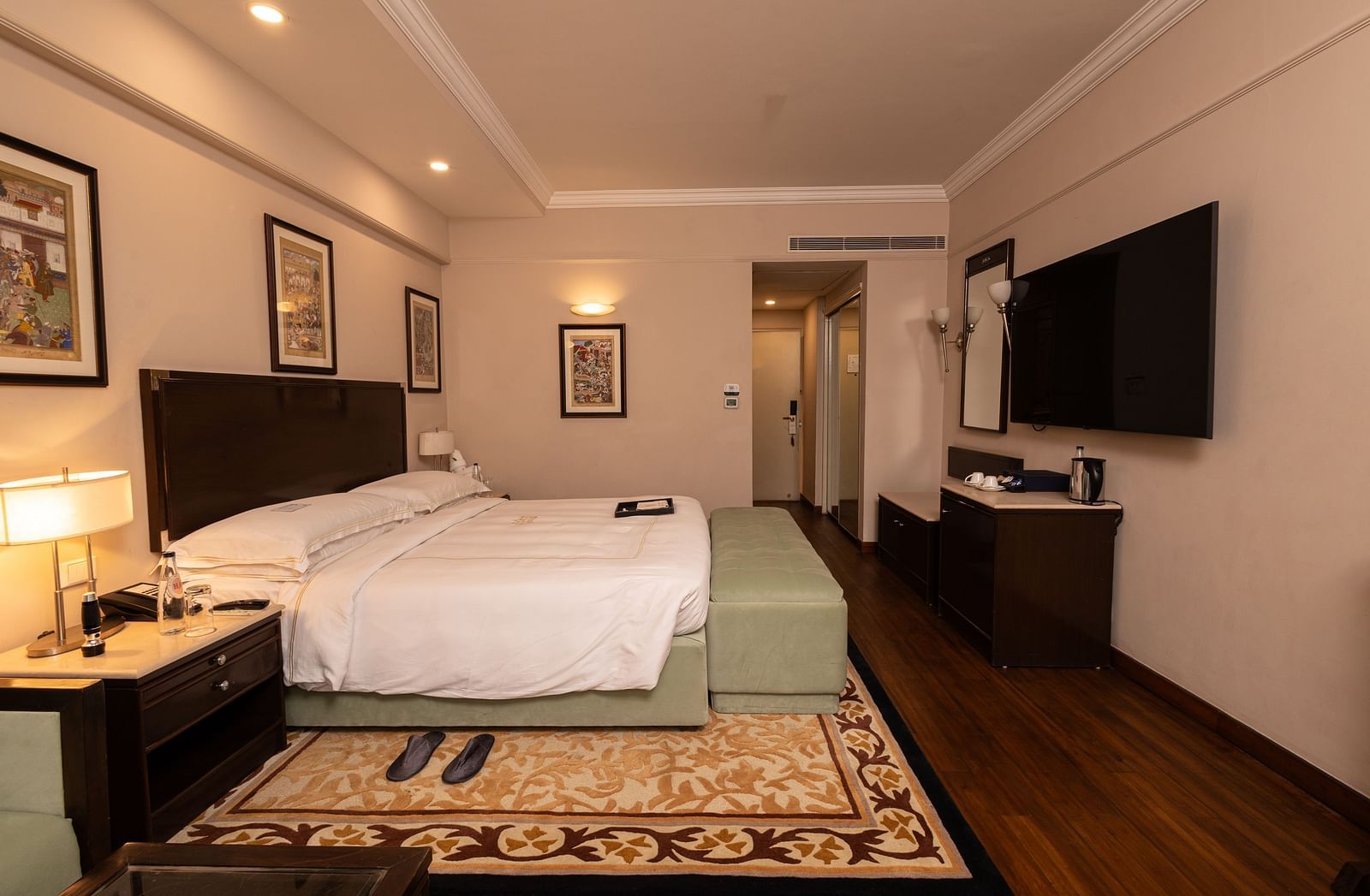 image of a brightly lit room with a king size bed and a wall mounted television placed opposite to the bed at our heritage balcony room - image of the heritage balcony room with sleek interiors and a a plush king size bed - The Claridges New Delhi