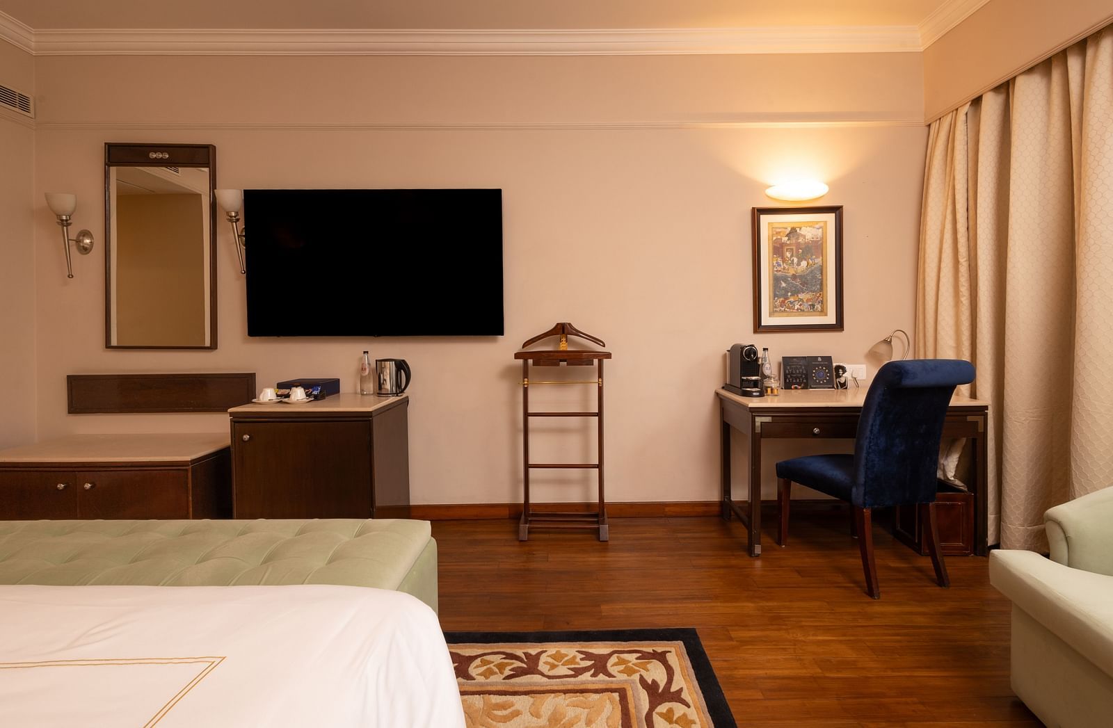 image of the heritage balcony room with a wall mounted tv and a work desk with a blue chair - image of the heritage balcony room with sleek interiors and a a plush king size bed - The Claridges New Delhi