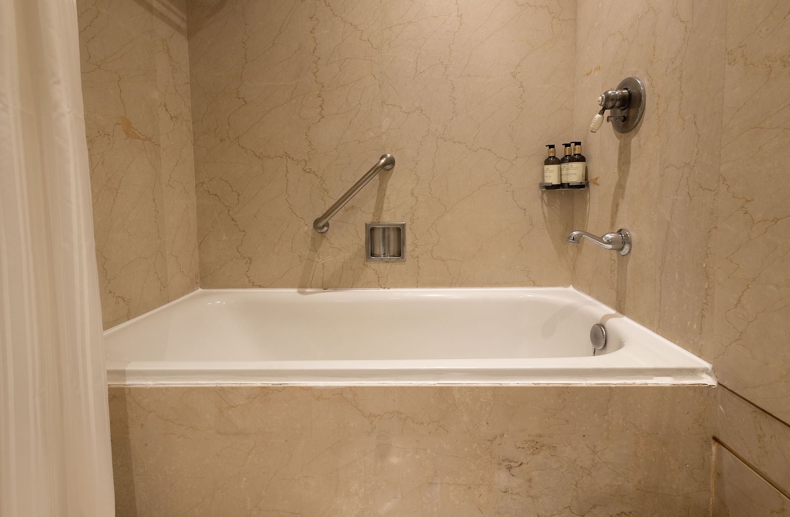 image of a bathtub with a curtain at our heritage balcony room with beige tiles -The Claridges New Delhi