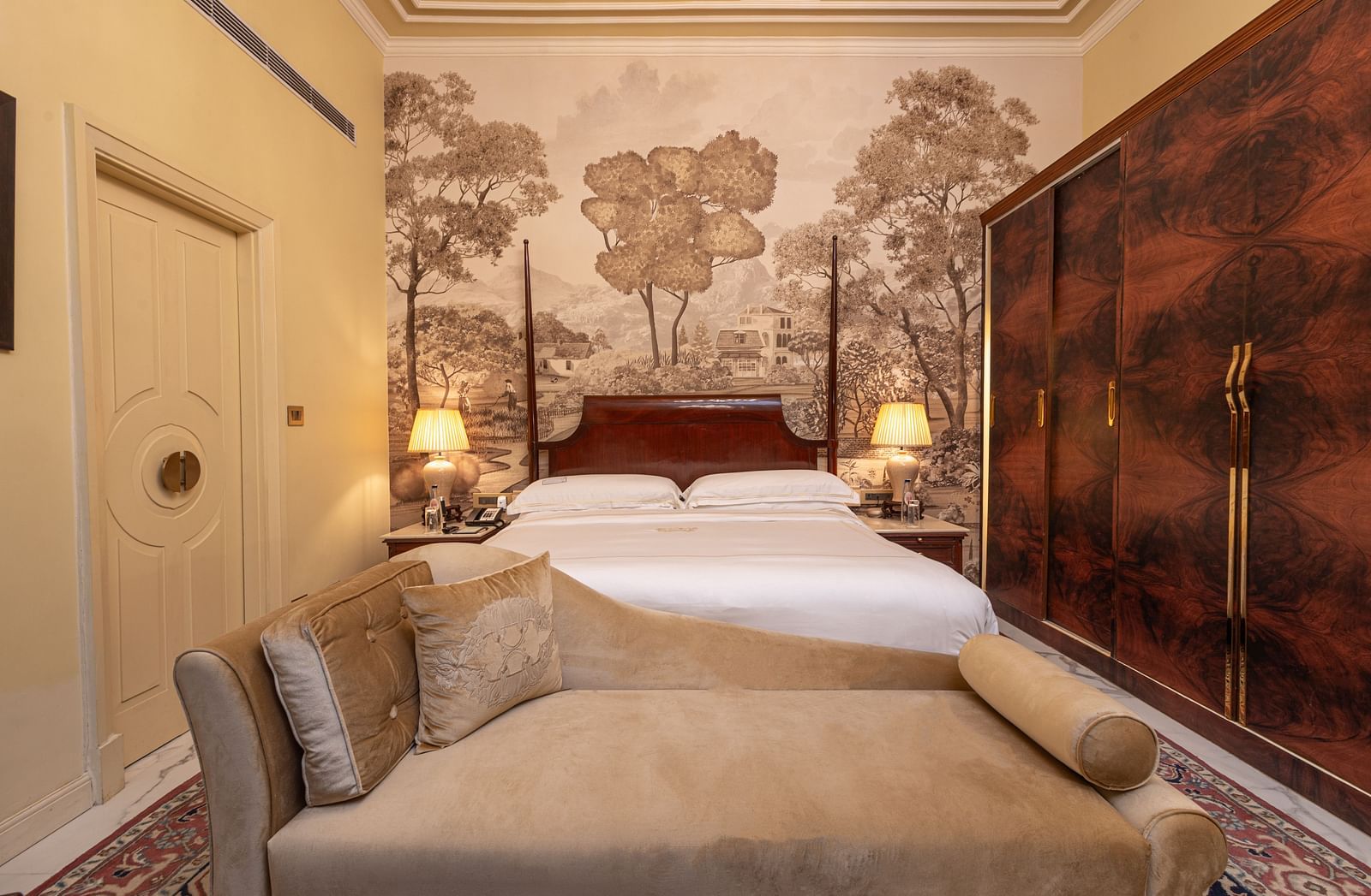 front view of the king size bed at the heritage room with a golden toned sofa with cushions over it - The Claridges New Delhi