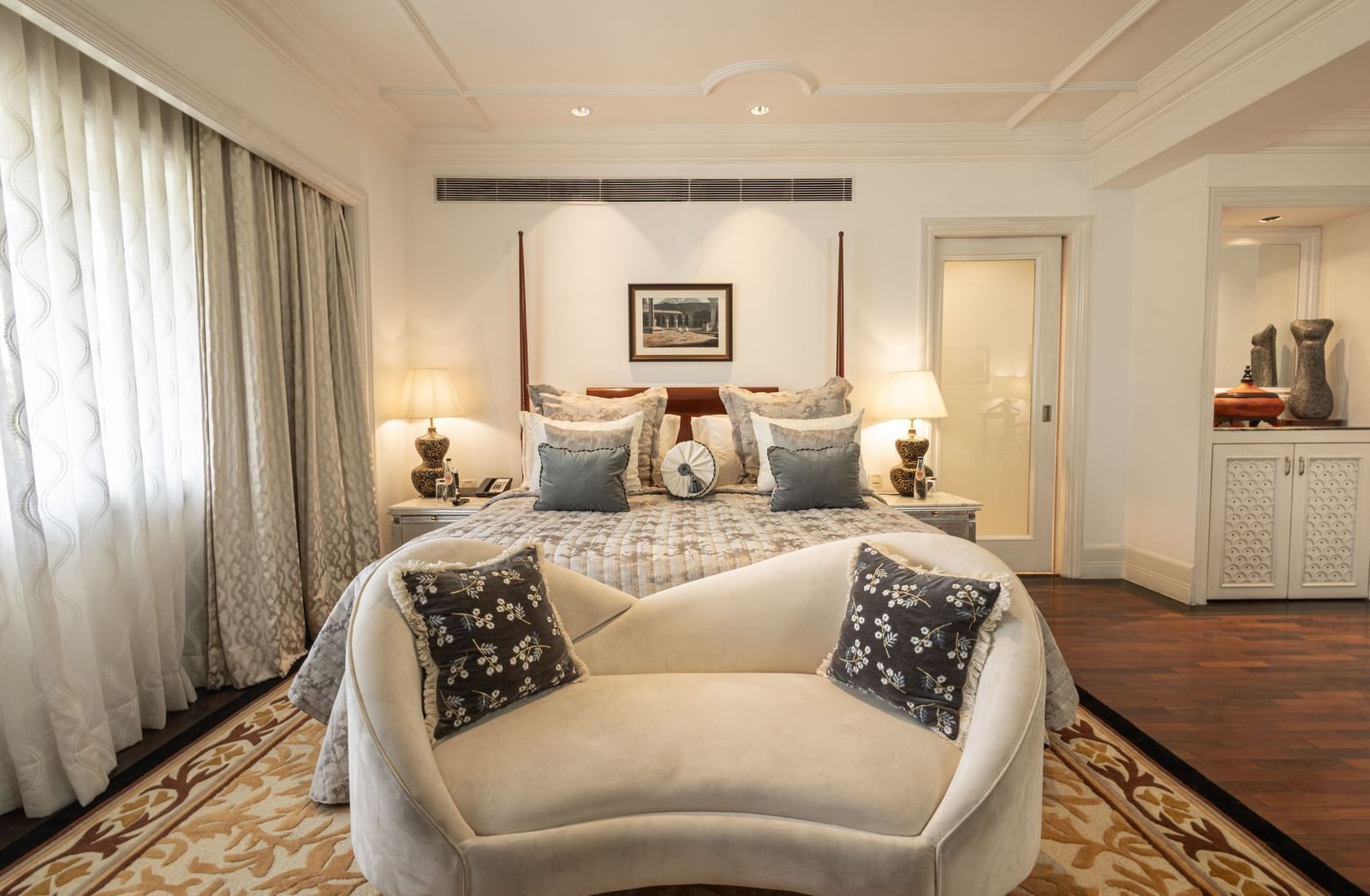 The Claridges New Delhi king-size bed is draped in white and gold fabrics with a decorative bench at the foot.