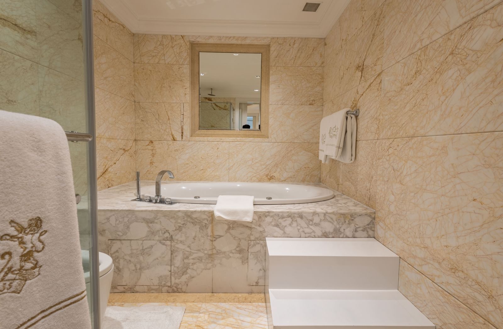 The Claridges New Delhi elegant marble bathroom has a large built-in bathtub and a mirror above.