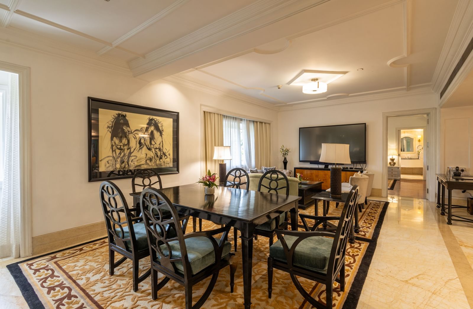 The Claridges New Delhi formal dining room is set with a dark table, black chairs, and a painting on the wall.