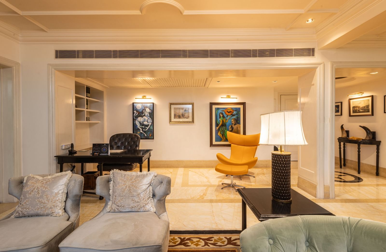 The Claridges New Delhi bright, luxurious sitting room is furnished with white sofas and a prominent yellow armchair.