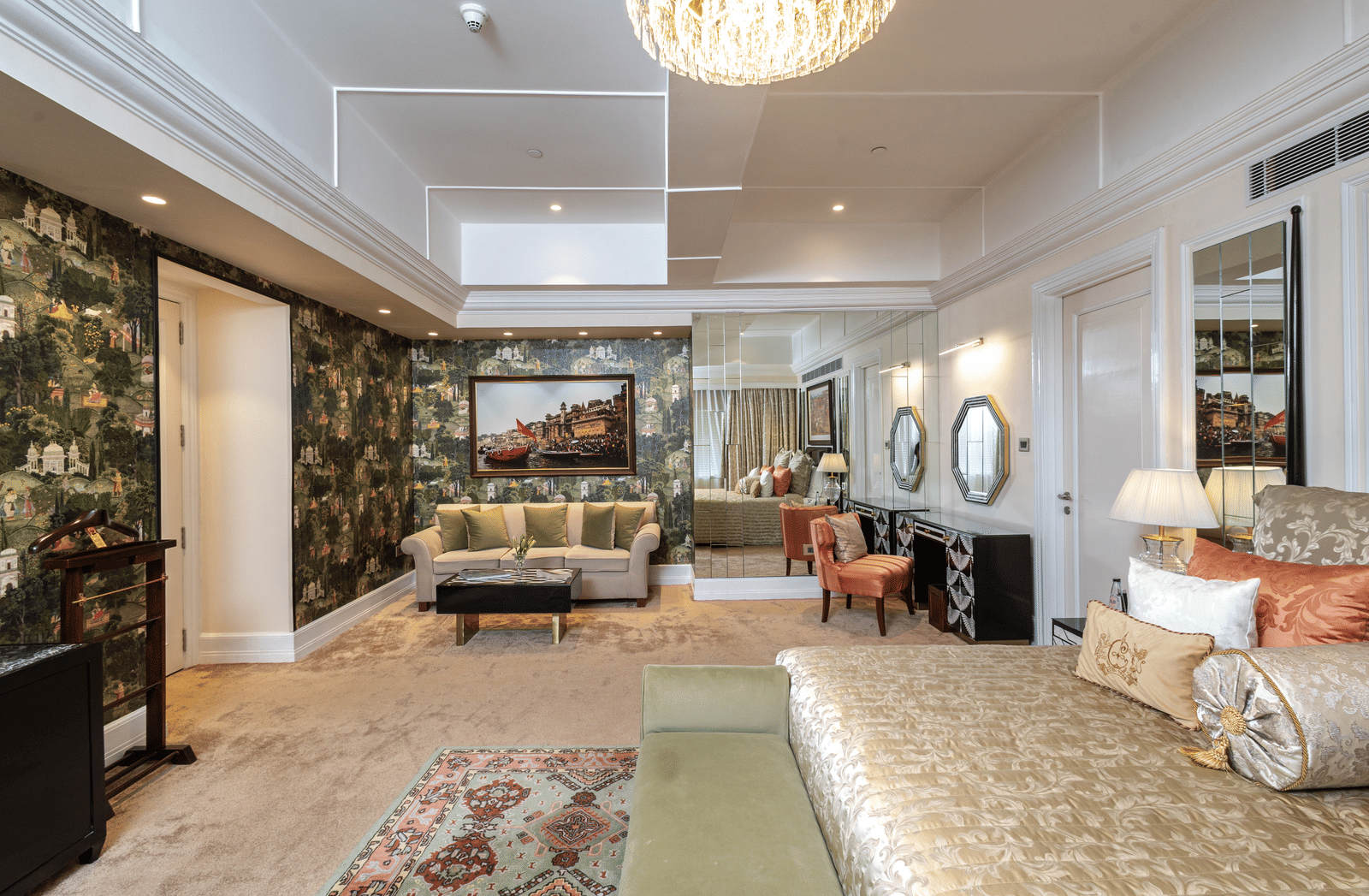 Presidential Suite bedroom featuring a king size bed, bedside tables, television, upholstered seating, and a large patterned area rug at The Claridges New Delhi.