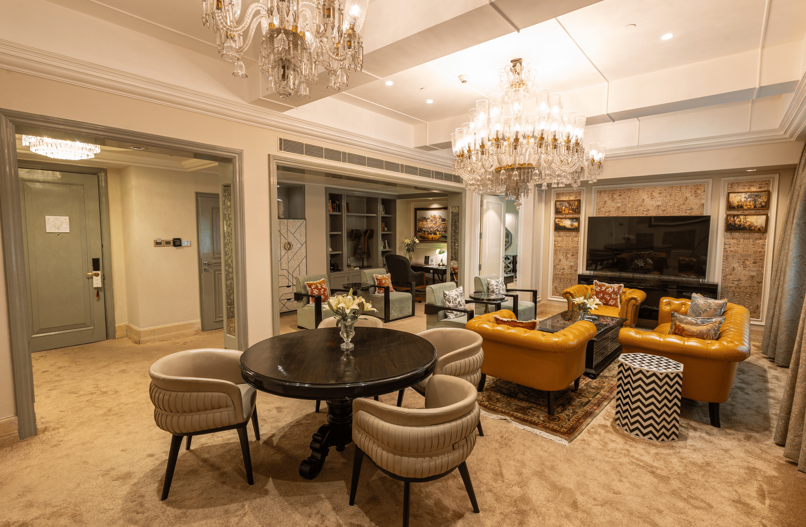 The living area of Presidential Suite featuring a round coffee table, upholstered armchairs, a sofa, floor lamp, and chandelier at The Claridges New Delhi.