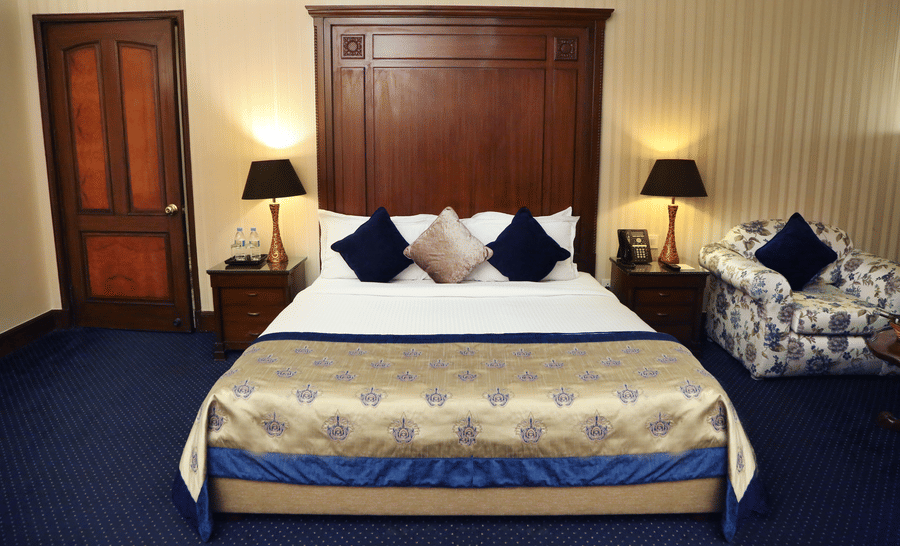 Premium Rooms at The Bristol Hotel Gurgaon, with a large bed, spreads, pillows, lamps, a door, and a cushion.